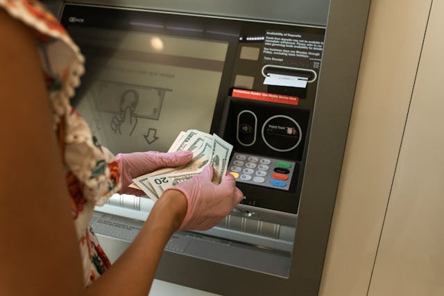 Person wearing gloves while holding money in front of an ATM